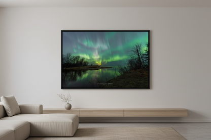 Large fine art landscape print of dramatic sweeping green aurora curtains bursting across the sky reflected in the calm Misery River with bare trees silhouetted and warm moonrise glow on the horizon Michigan Upper Peninsula April 24 2023 at 1:00am displayed in modern living room
