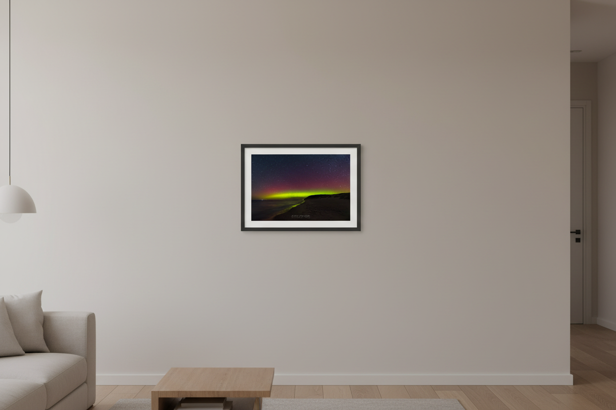 Small fine art print of crimson aurora and lime green horizon band over Lake Michigan from North Bar Lake beach with sweeping curved shoreline and forested headland bluff silhouette Sleeping Bear Dunes displayed in modern living room