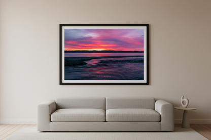 Large fine art landscape print of explosive crimson magenta and orange sunrise sky over Shalda Creek and Lake Michigan with calm water reflections and sandy foreground spit March 9 2023 displayed in modern living room