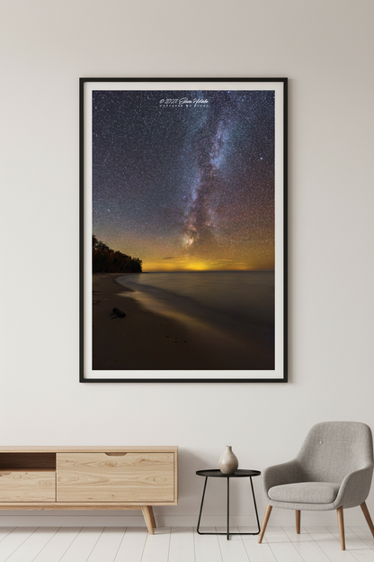 Large fine art portrait print of the Milky Way rising over Lake Michigan from Christmas Cove Beach Northport Michigan October 22 2022 at 10:08pm with warm golden horizon glow and sandy beach foreground displayed in modern living room