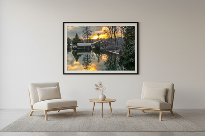 Large fine art landscape print of snowy Christmas boathouse scene with fiery golden sunrise reflecting in still water Leland Michigan December 2022 displayed in modern living room