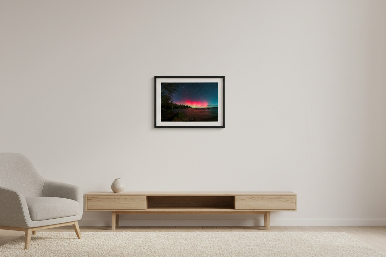 Small fine art print of broad crimson red aurora mass with green teal horizon glow over Lake Leelanau wooded shoreline from Leland Michigan November 8 2024 wide panoramic view with water reflection displayed in modern living room