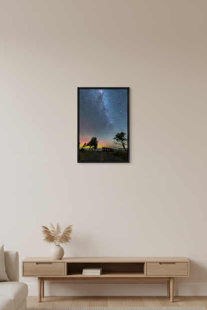 Small fine art portrait print of Milky Way arching overhead with thousands of stars faint aurora glow of pink green and yellow on horizon two tree silhouettes flanking glowing red barn along rural road at Glen Haven Michigan July 31 2022 displayed in modern living room
