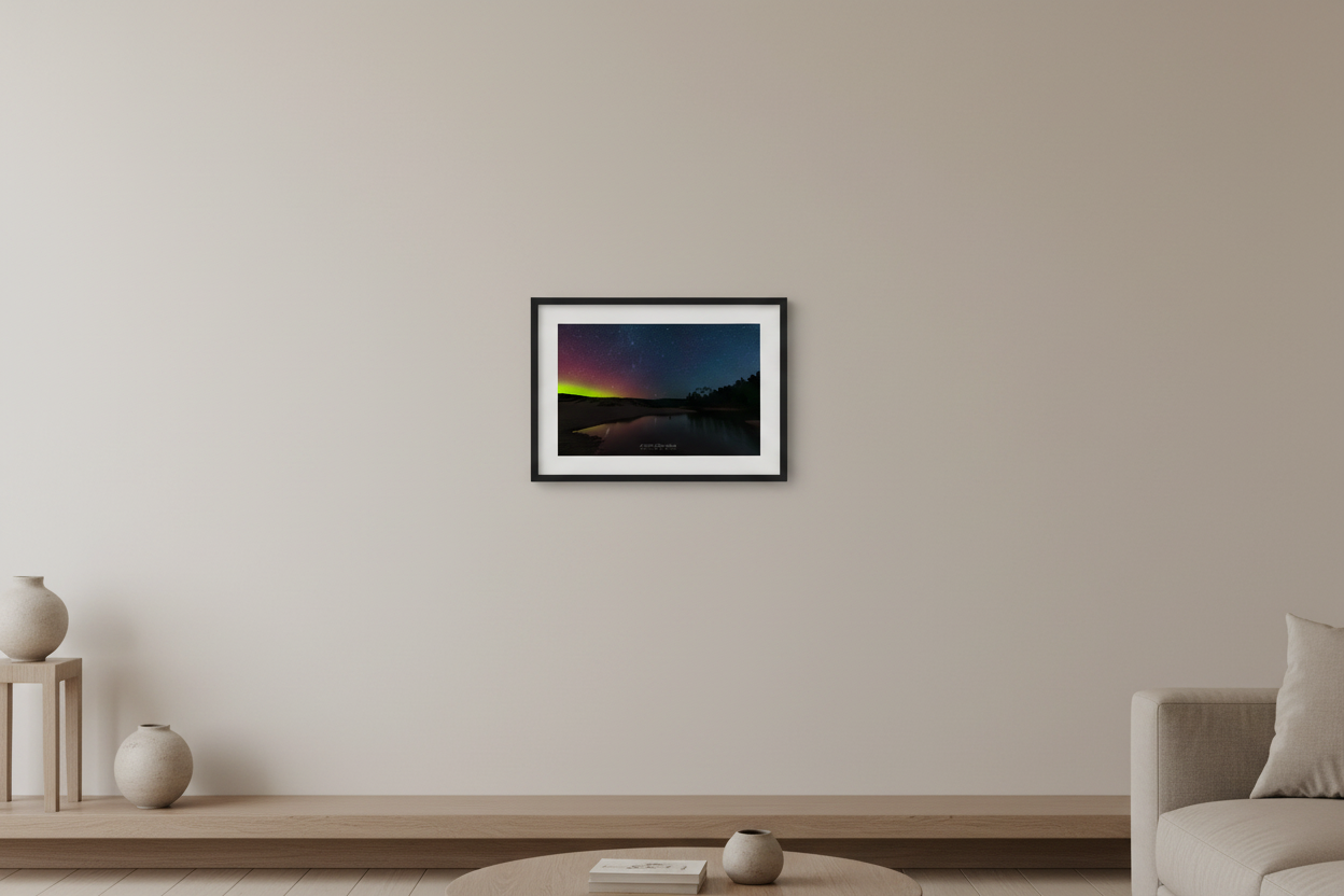 Small fine art print of aurora borealis confined to left half of frame with lime green horizon glow and crimson sky over inland pond with dark conifer treeline right and deep blue starfield North Bar Lake Sleeping Bear Dunes displayed in modern living room