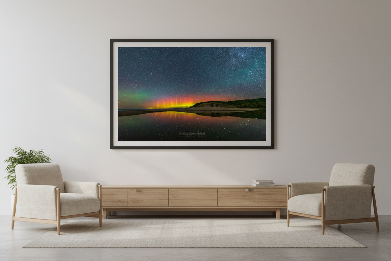 Large fine art landscape print of vivid red orange and yellow Northern Lights pillars perfectly mirrored in glassy North Bar Lake with sand dunes and forested bluff silhouetted on right and star-filled sky at Sleeping Bear Dunes Michigan August 31 2022 displayed in modern living room