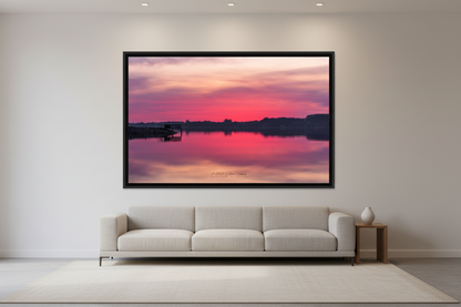 Large fine art landscape print of a vivid magenta and pink sunrise perfectly reflected in glassy calm water at Sutton's Bay with silhouetted dock and treeline Leelanau County Michigan March 12 2024 displayed in modern living room