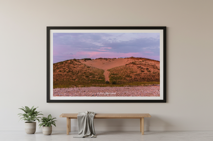 Large fine art print of warm terracotta sand dune face with rocky pebble beach foreground and soft lavender purple sky at Sleeping Bear Point MI displayed in modern living room