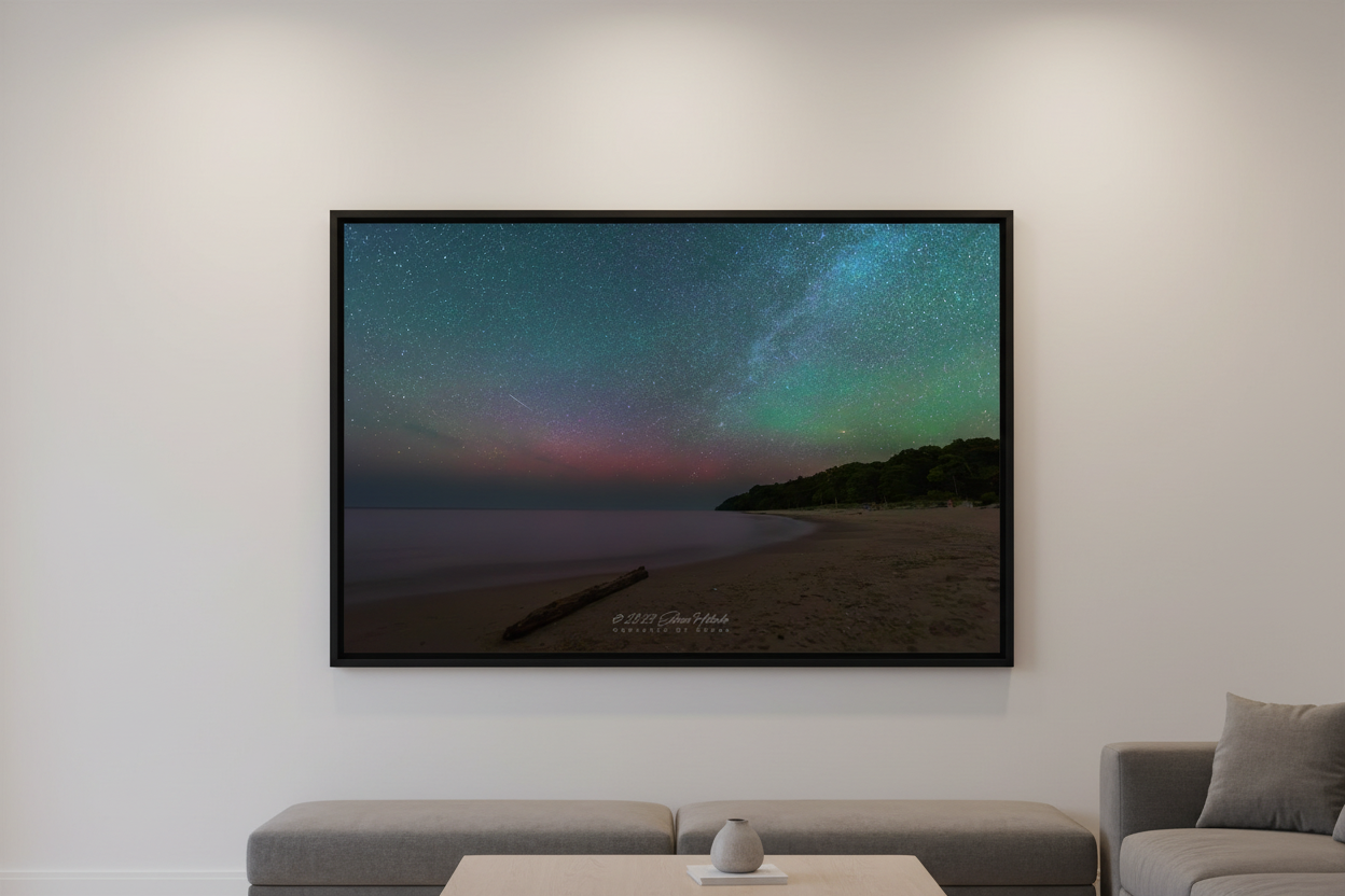 Large fine art landscape print of the Milky Way and pink green aurora over Lake Michigan beach near Leland Michigan with sandy shore driftwood log and dark forested bluff June 21 2023 displayed in modern living room