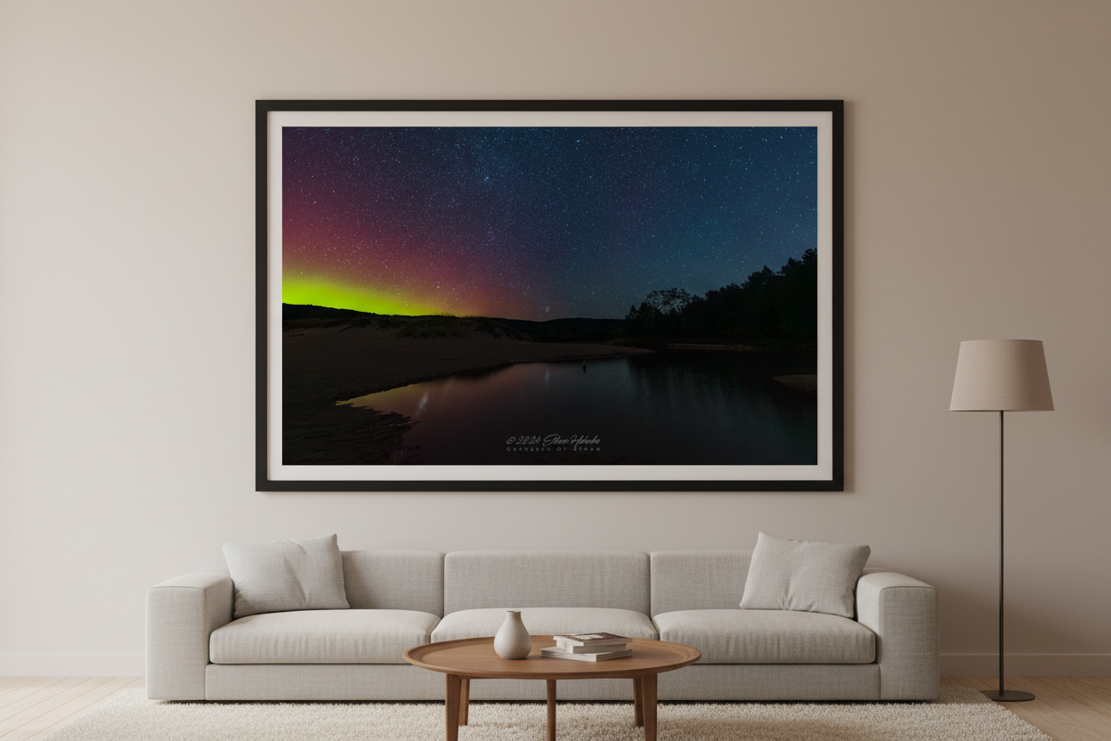 Large fine art print of aurora borealis confined to left half of frame with lime green horizon glow and crimson sky over inland pond with dark conifer treeline right and deep blue starfield North Bar Lake Sleeping Bear Dunes displayed in modern living room