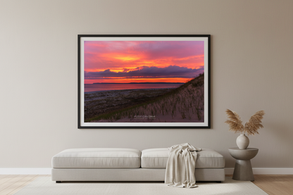 Large fine art print of warm pink orange sunrise over Sleeping Bear Bay from dune face foreground with sandy beach below and prominent headland silhouette displayed in modern living room