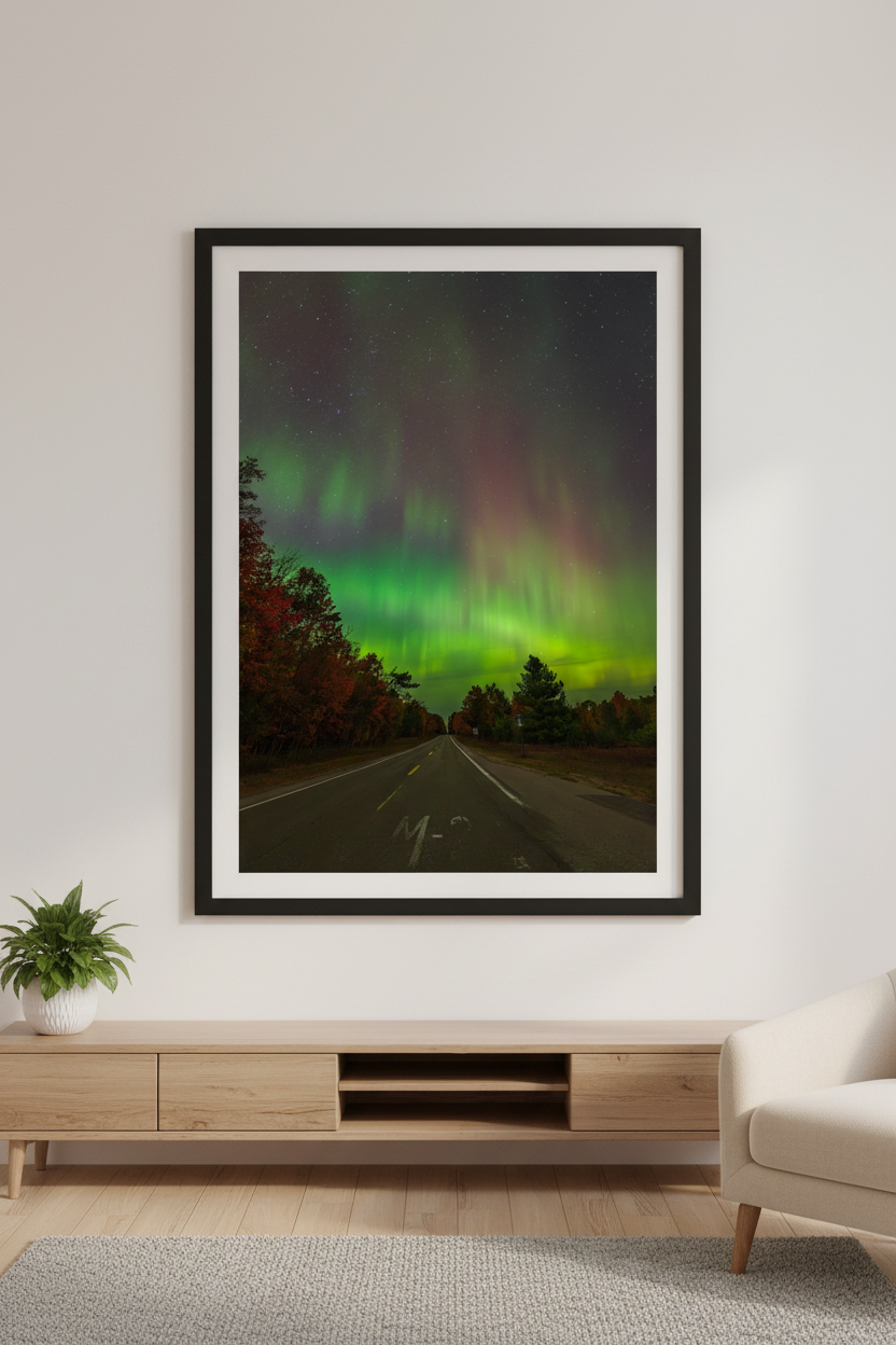 Large fine art portrait print of aurora borealis erupting above M-22 highway road with autumn foliage trees and vivid green and crimson red aurora rays at 4:15am October 11 2024 displayed in modern living room