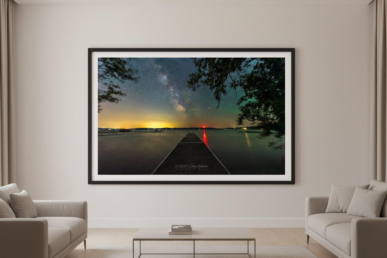 Large fine art landscape print of the Milky Way rising above a dock extending over glassy Lake Leelanau Michigan with golden horizon glow red light reflection and pine trees June 22 2023 displayed in modern living room