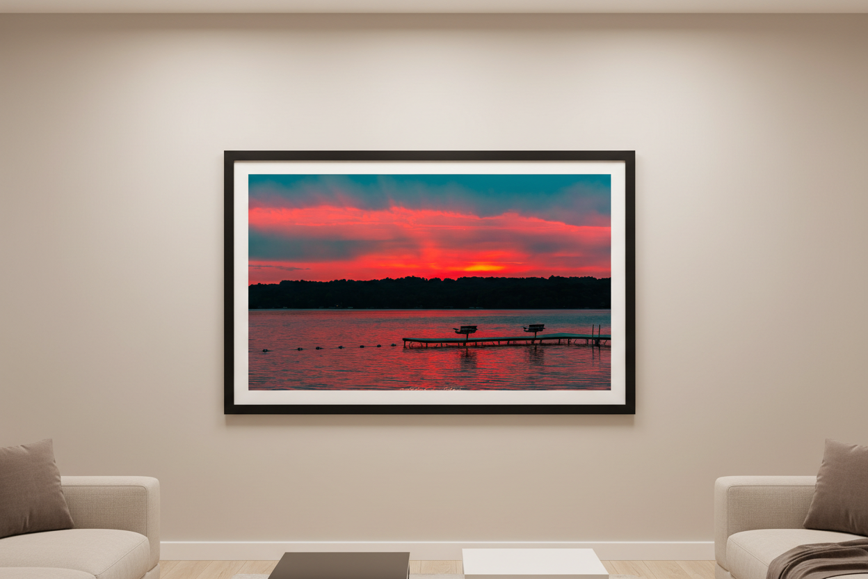 Large fine art print of Lake Leelanau fire sunset with visible golden sun orb at treeline centered L-shaped swimming dock with benches magenta pink sky teal storm clouds wide open water foreground swim rope buoy line Leland Michigan displayed in modern living room