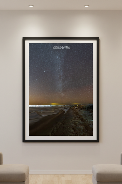 Large fine art portrait print of Milky Way rising over Lake Michigan beach and rocky breakwall with warm amber horizon glow at Leland Michigan February 11 2023 displayed in modern living room