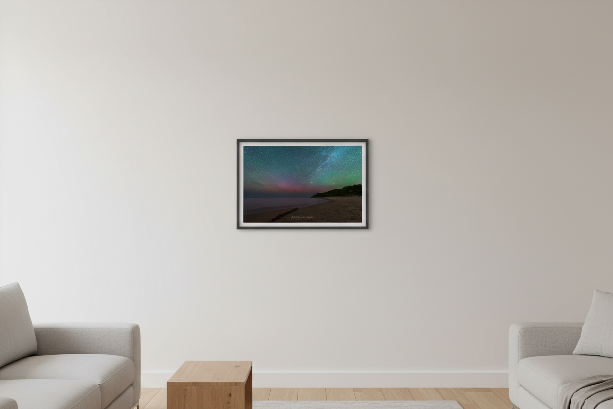 Small fine art landscape print of the Milky Way and pink green aurora over Lake Michigan beach near Leland Michigan with sandy shore driftwood log and dark forested bluff June 21 2023 displayed in modern living room