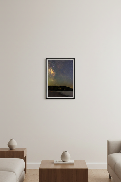 Small fine art portrait print of the Milky Way core over Leelanau Peninsula at Christmas Cove Beach Northport Michigan September 18 2023 at 9:08pm with warm amber horizon glow and silhouetted tree line across calm water displayed in modern living room