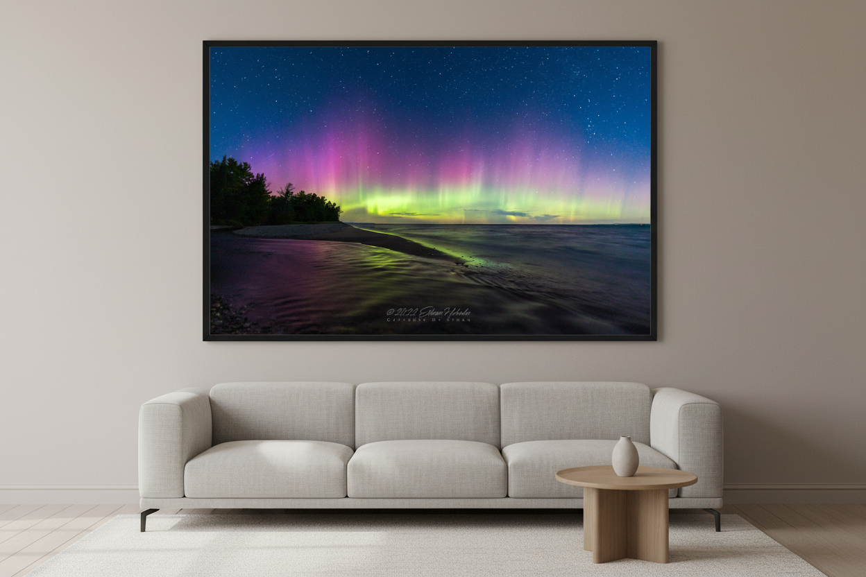 Large fine art landscape print of full-spectrum Northern Lights with vivid green base bursting into tall pink and purple pillars over Shalda Creek sandy beach shoreline with dark tree silhouettes and calm open water at Lake Michigan Michigan September 4 2022 displayed in modern living room