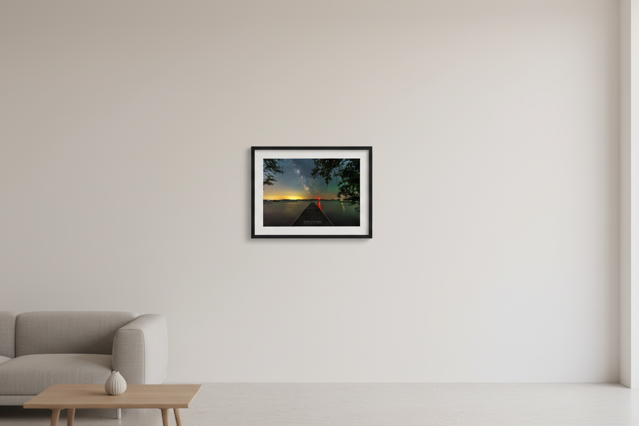 Small fine art landscape print of the Milky Way rising above a dock extending over glassy Lake Leelanau Michigan with golden horizon glow red light reflection and pine trees June 22 2023 displayed in modern living room