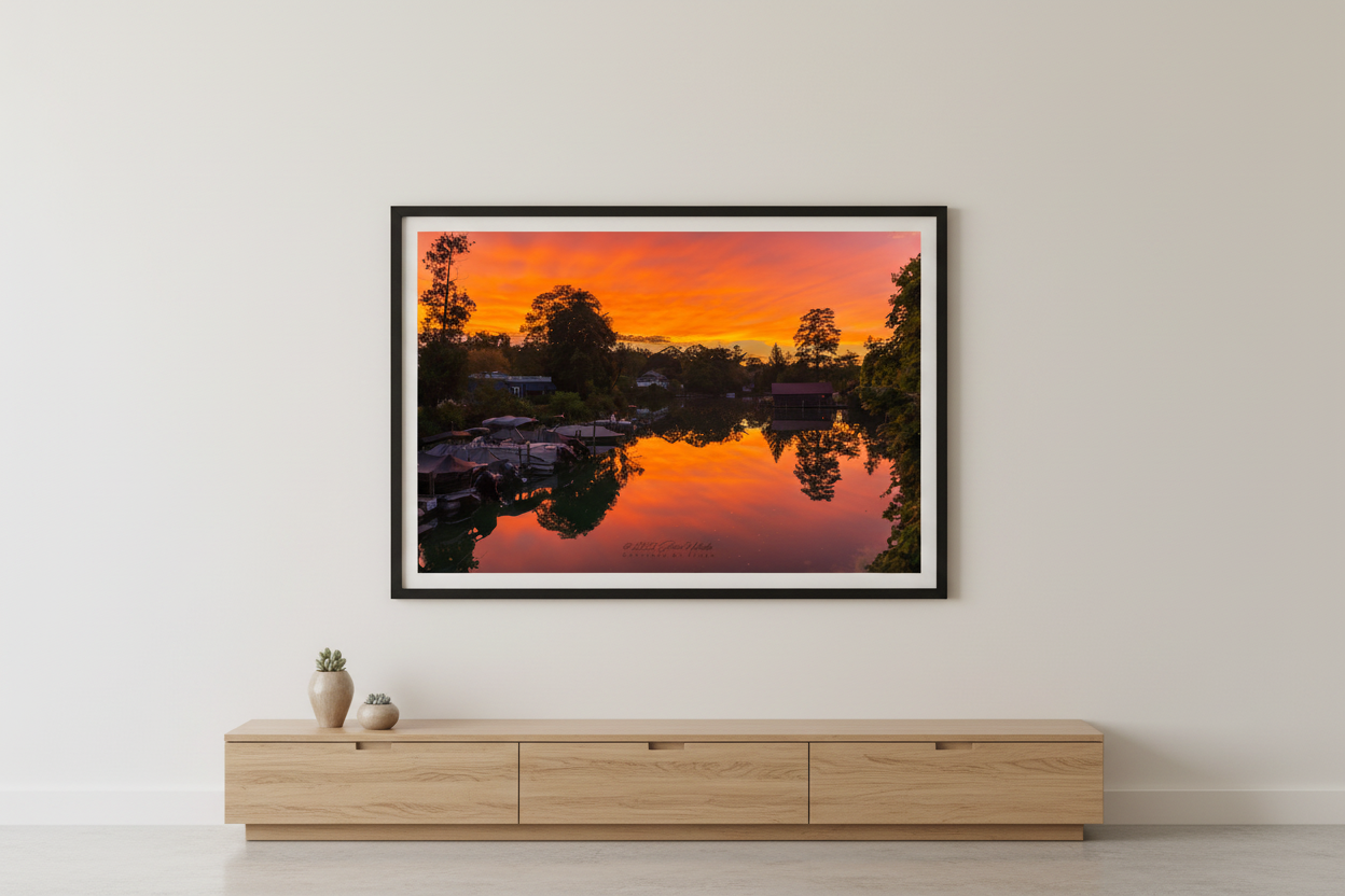 Large fine art landscape print of blazing orange red sunset perfectly mirrored in glassy Leland River with boat docks and tree silhouettes Michigan September 2022 displayed in modern living room
