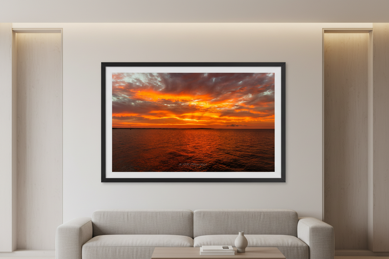 Large fine art print of blazing orange amber fire sunrise over open Grand Traverse Bay with towering dramatic storm cloud architecture and brilliant yellow white sun core displayed in modern living room