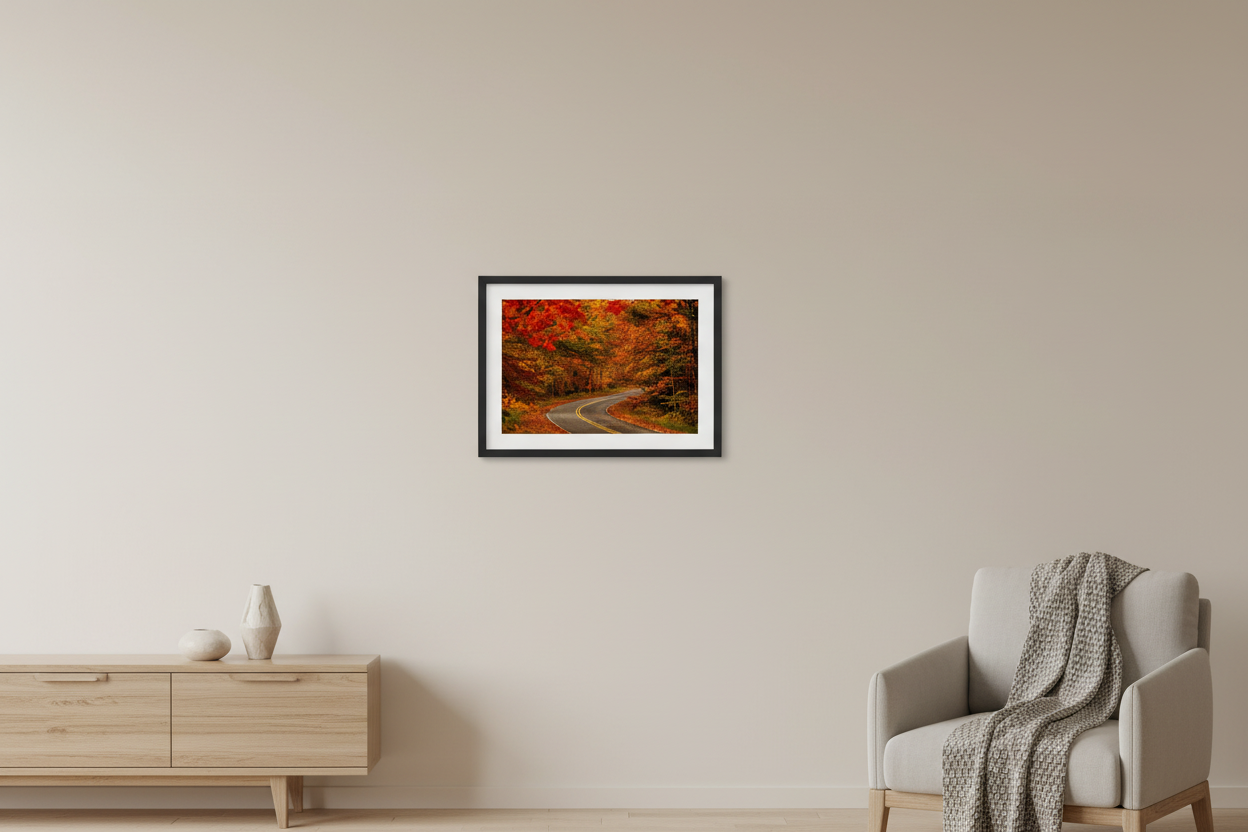 Small fine art print of winding two-lane road through a crimson red and burnt orange fall foliage tunnel on Gills Pier Road in northern Michigan with telephoto compression and fallen leaf carpet displayed in modern living room