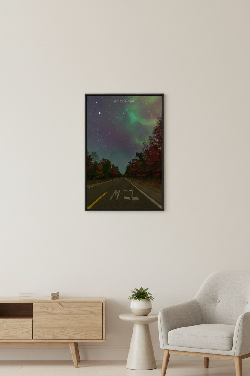 Small fine art portrait print of M-22 road marking on highway looking south flanked by vivid autumn red foliage with soft green aurora wisps and star-filled sky including Orion and Pleiades at 4:14am October 11 2024 displayed in modern living room