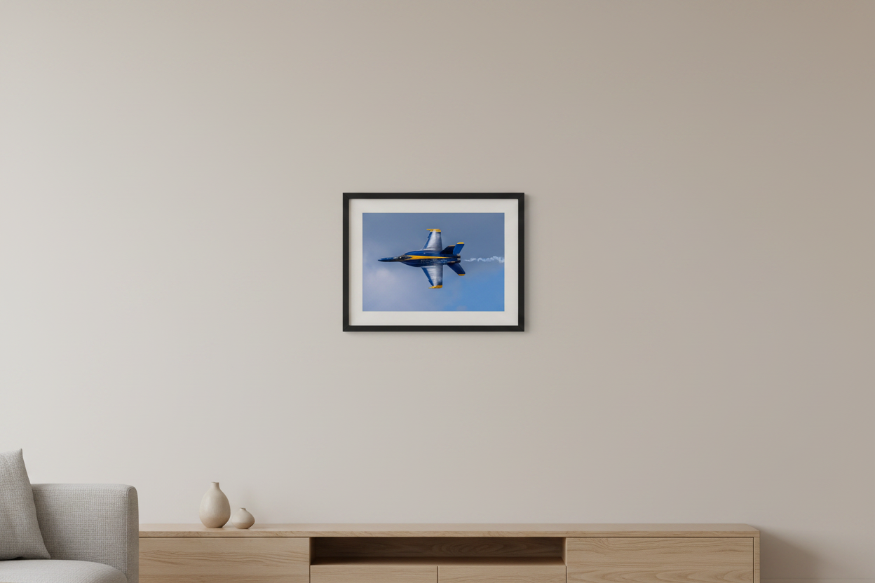 Small fine art landscape print of a single Blue Angels F/A-18 Super Hornet photographed belly-up in a knife-edge roll with dramatic wing vapor condensation cloud against a blue sky at the 2024 Traverse City Cherry Festival Airshow displayed in modern living room