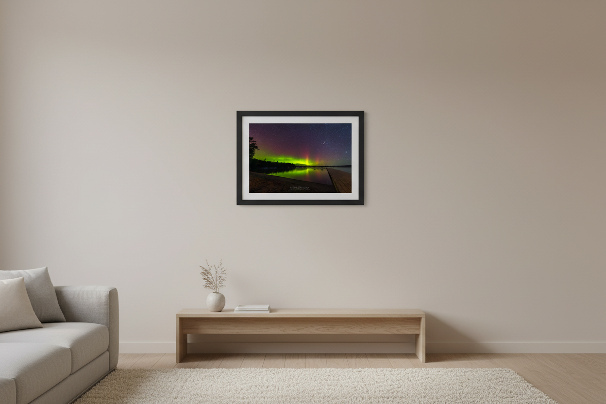 Small fine art print of vertical aurora pillars lime green and crimson over Lake Leelanau with wooden dock foreground deciduous treeline and glassy lake reflection meteor streak Leland Michigan displayed in modern living room