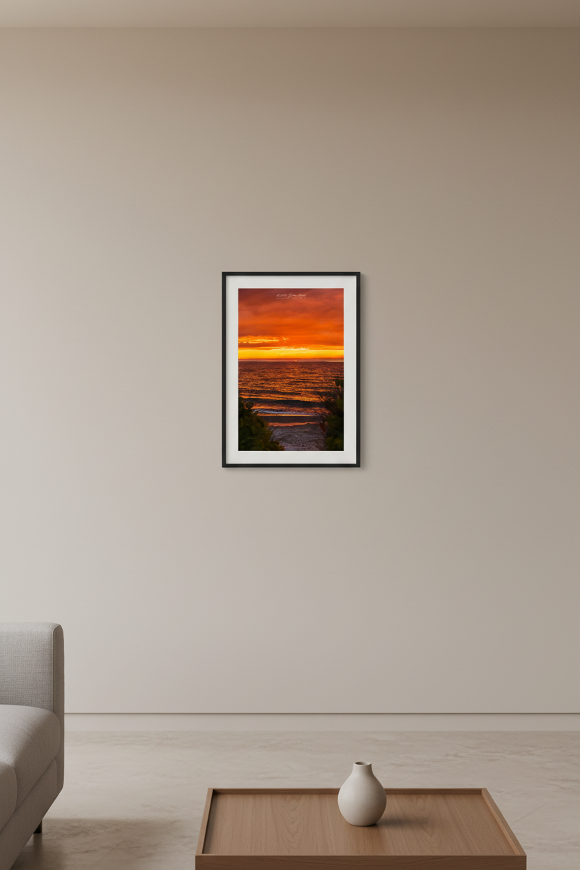 Small fine art portrait print of blazing all-red orange sky sunset with golden wave reflections and lush green foliage beach path framing foreground Leland Lake Michigan July 2024 displayed in modern living room
