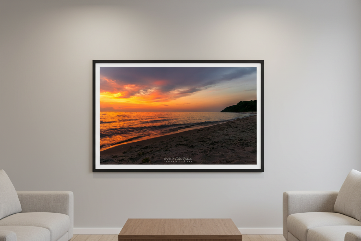 Large fine art landscape print of a blazing orange sunset over Lake Michigan with sandy beach foreground and dark tree-covered headland silhouette at Leland Michigan July 2024 displayed in modern living room