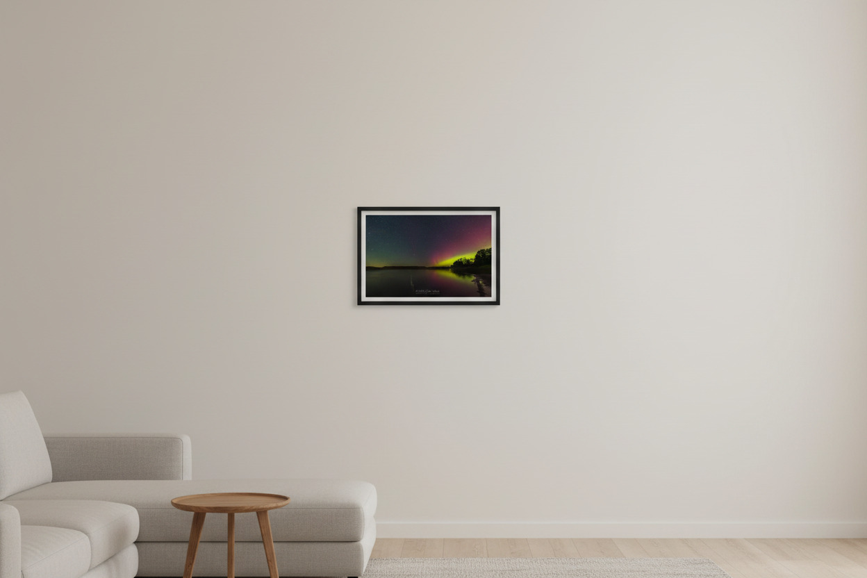 Small fine art print of crimson red and lime green Northern Lights aurora reflecting in glassy North Bar Lake with deciduous treeline silhouette and rolling hill horizon displayed in modern living room