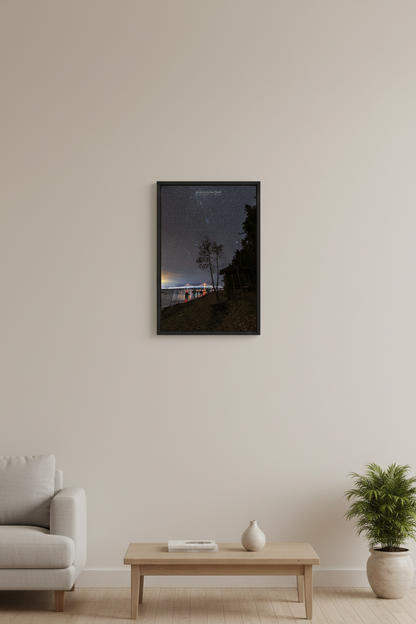 Small fine art portrait print of the Mackinac Bridge illuminated at night with colorful lights reflecting in the Straits of Mackinac silhouetted tree and cabin foreground star filled sky Mackinaw City September 30 2022 displayed in modern living room