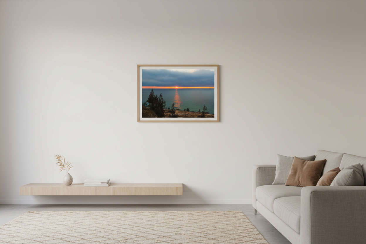 Small fine art landscape print of glowing orange sunset stripe on horizon with golden reflection path across turquoise Lake Michigan viewed from Empire Bluffs overlook with silhouetted evergreens Sleeping Bear Dunes April 2023 displayed in modern living room
