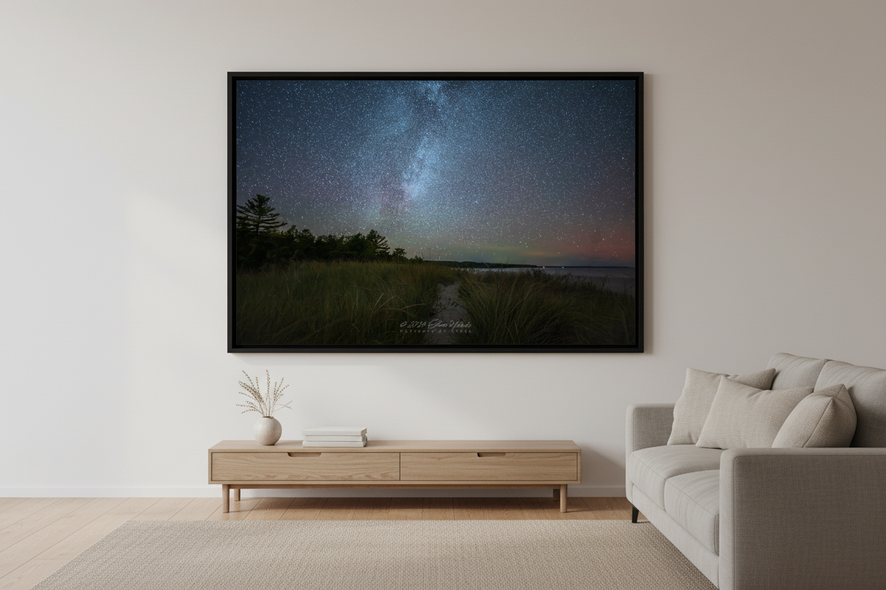 Large fine art print of Milky Way galaxy over Bohemian Road Beach Michigan with aurora borealis pink red glow on horizon sandy beach path tall beach grass pine tree silhouettes calm water Oct 5 2024 displayed in modern living room