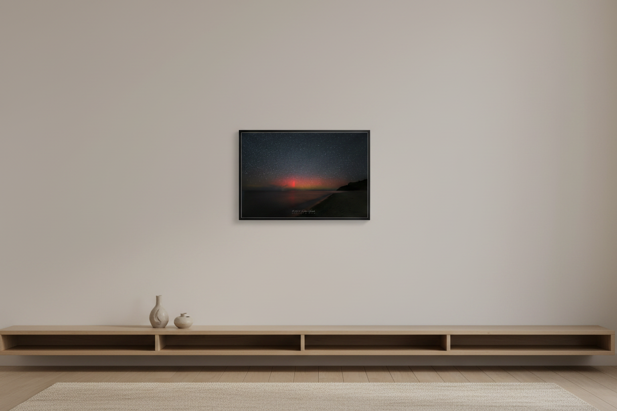 Small fine art print of wide diffuse aurora borealis red and green-yellow airglow band over Lake Michigan from North Street Beach Leland Michigan curved sandy beach dark tree-lined headland lower right long exposure calm water Oct 5 2024 3:18am displayed in modern living room