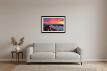 Small fine art landscape print of surreal pink magenta and orange sunset sky over snow-dusted orange sand dune and vast snow-covered Sleeping Bear Dunes landscape with bare trees and Lake Michigan on horizon March 2023 displayed in modern living room