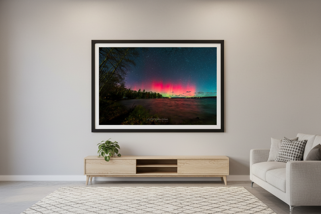 Large fine art print of broad crimson red aurora mass with green teal horizon glow over Lake Leelanau wooded shoreline from Leland Michigan November 8 2024 wide panoramic view with water reflection displayed in modern living room