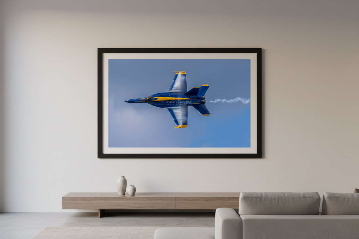 Large fine art landscape print of a single Blue Angels F/A-18 Super Hornet photographed belly-up in a knife-edge roll with dramatic wing vapor condensation cloud against a blue sky at the 2024 Traverse City Cherry Festival Airshow displayed in modern living room
