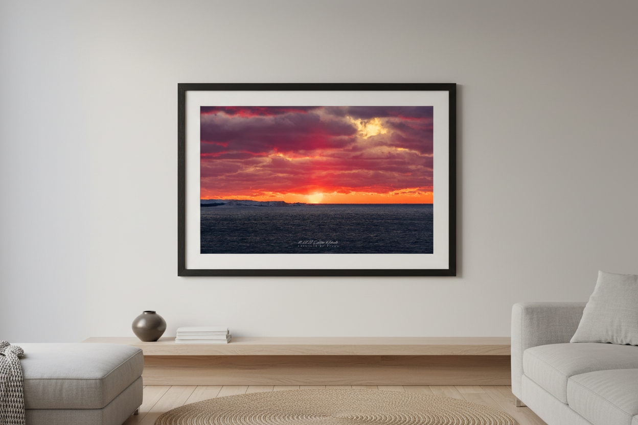 Large fine art landscape print of fiery crimson and purple sunset color explosion over snow-covered Sleeping Bear Point with dark choppy Lake Michigan water January 2023 displayed in modern living room