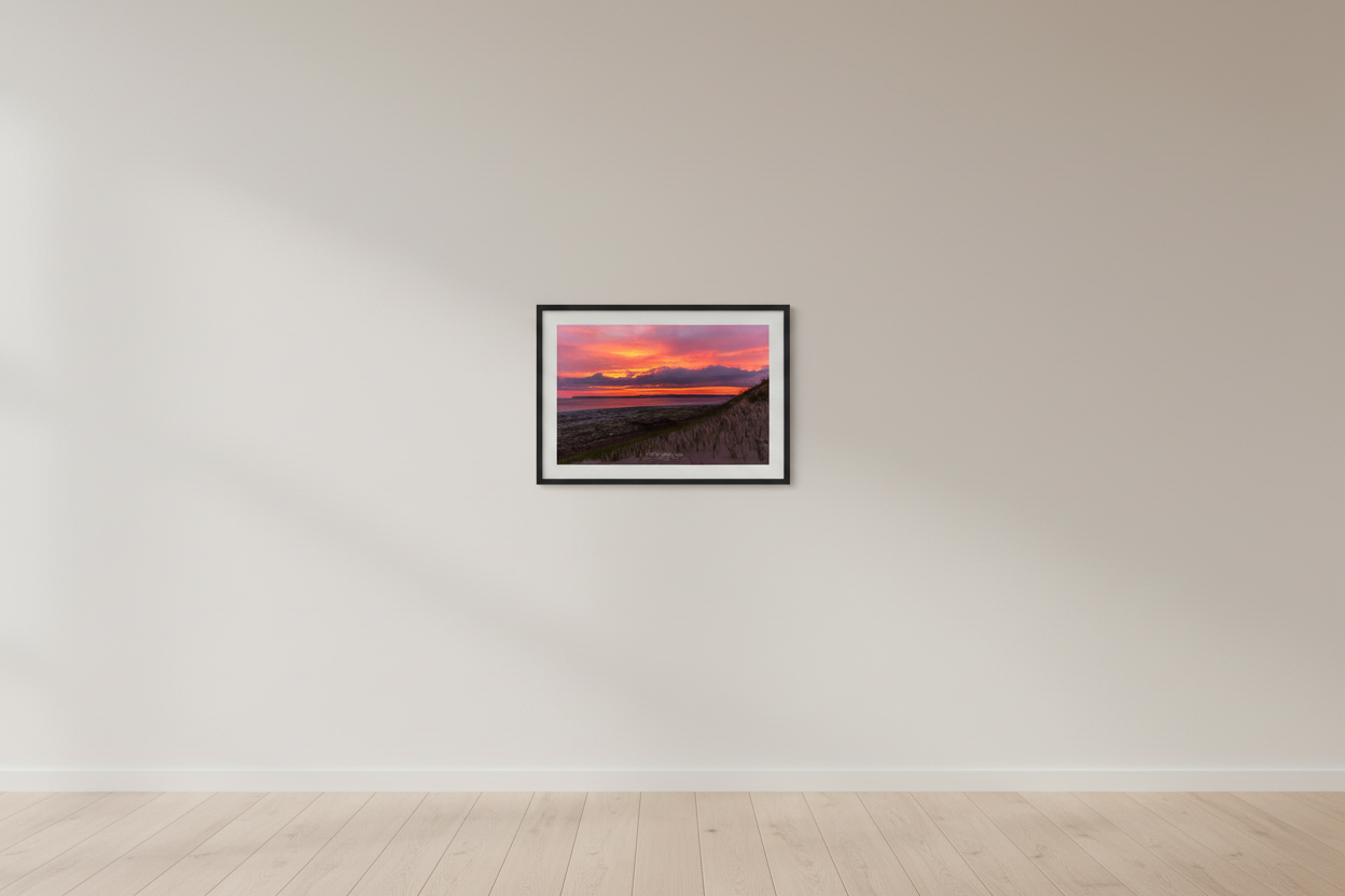 Small fine art print of warm pink orange sunrise over Sleeping Bear Bay from dune face foreground with sandy beach below and prominent headland silhouette displayed in modern living room