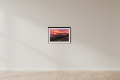 Small fine art print of warm pink orange sunrise over Sleeping Bear Bay from dune face foreground with sandy beach below and prominent headland silhouette displayed in modern living room