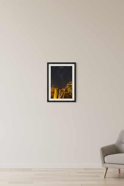 Small fine art portrait print of star-filled night sky over Fishtown docks Leland River with warm golden dock lighting and DAM Candy Store Leland Michigan February 11 2023 displayed in modern living room
