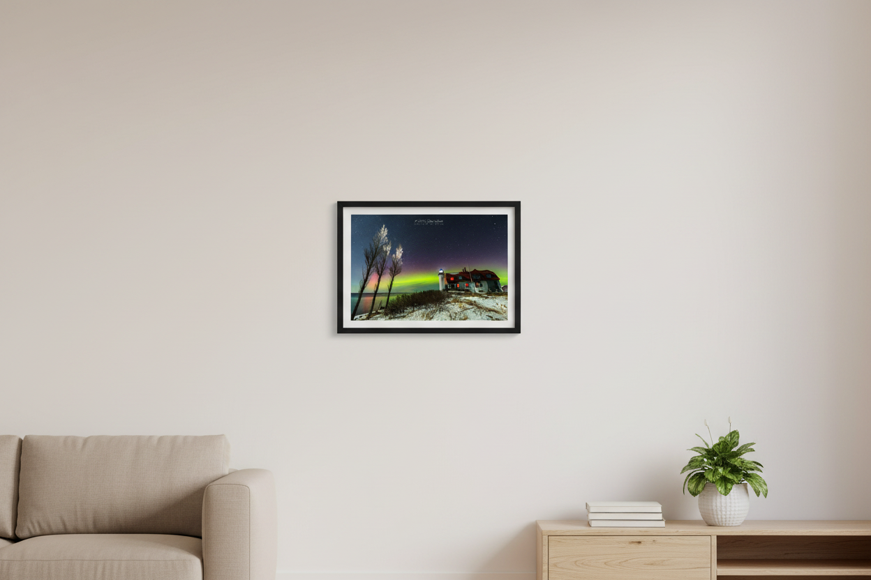 Small fine art landscape print of vivid green and pink aurora borealis glowing above Point Betsie Lighthouse with snow-covered ground and bare birch trees on Lake Michigan February 27 2023 displayed in modern living room