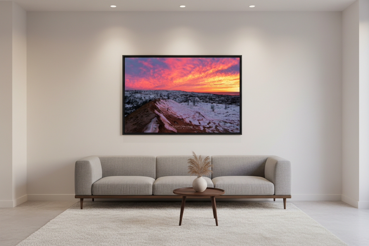 Large fine art landscape print of surreal pink magenta and orange sunset sky over snow-dusted orange sand dune and vast snow-covered Sleeping Bear Dunes landscape with bare trees and Lake Michigan on horizon March 2023 displayed in modern living room