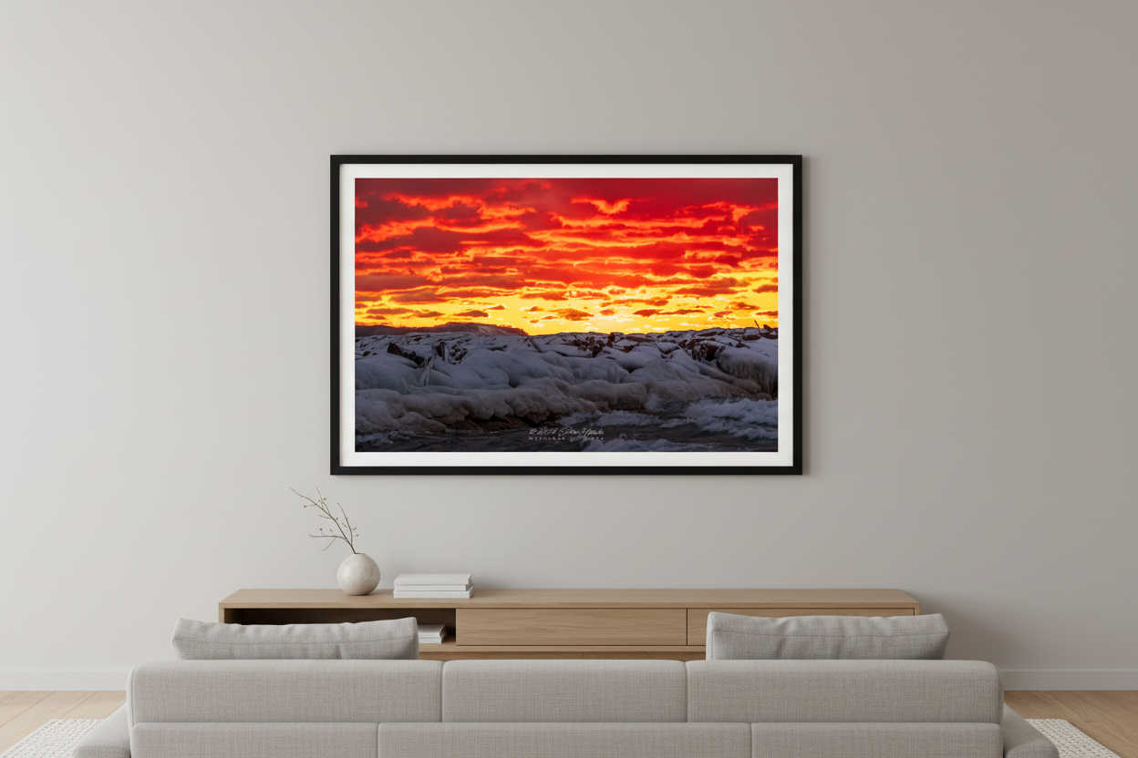 Large fine art landscape print of ice-encrusted Leland breakwall under a dramatic crimson and orange fire sunset sky with golden horizon glow Lake Michigan January 30 2023 displayed in modern living room