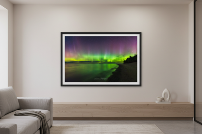 Large fine art landscape print of vivid green yellow and purple Northern Lights aurora borealis reflecting in calm Lake Michigan water at Christmas Cove Beach Northport Michigan September 18 2023 at 11:14pm displayed in modern living room