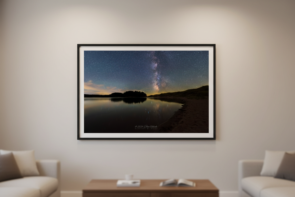 Large fine art print of Milky Way galaxy core rising over glassy North Bar Lake with island silhouette sandy dune shoreline and warm amber horizon glow Sleeping Bear Dunes displayed in modern living room