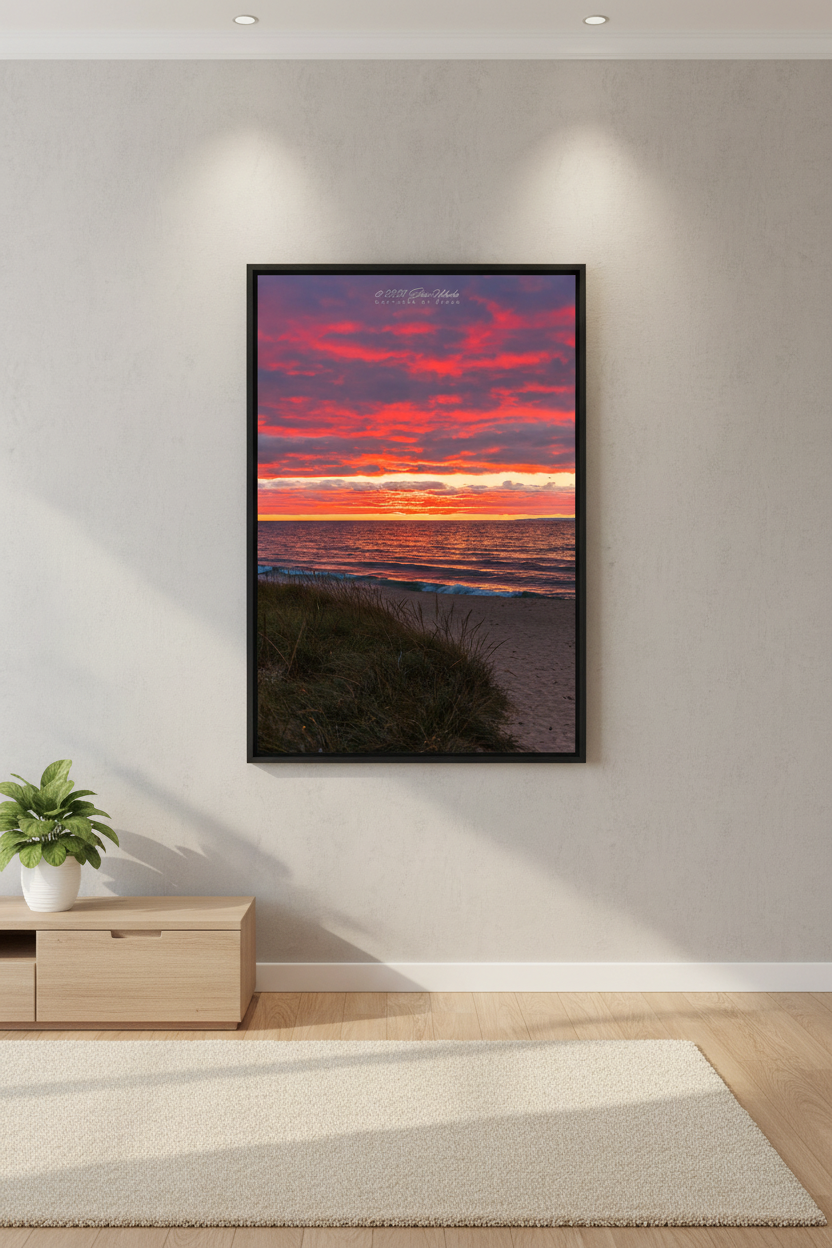 Large fine art portrait print of fiery red and magenta cloud explosion over Lake Michigan with dune grass foreground and gentle shoreline waves at Van's Beach Leland MI October 2023 displayed in modern living room