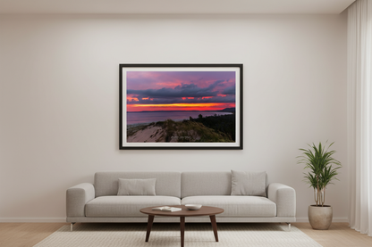 Large fine art print of peaceful purple magenta sunrise over Sleeping Bear Bay from elevated sand dune overlook at Sleeping Bear Point with dune grass foreground and blazing orange horizon band displayed in modern living room