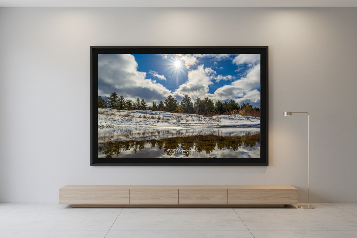 Large fine art landscape print of snow-covered sand dunes with pine treeline and brilliant sunstar reflected in a calm tidal channel at Good Harbor Beach Sleeping Bear Dunes National Lakeshore January 29 2023 displayed in modern living room
